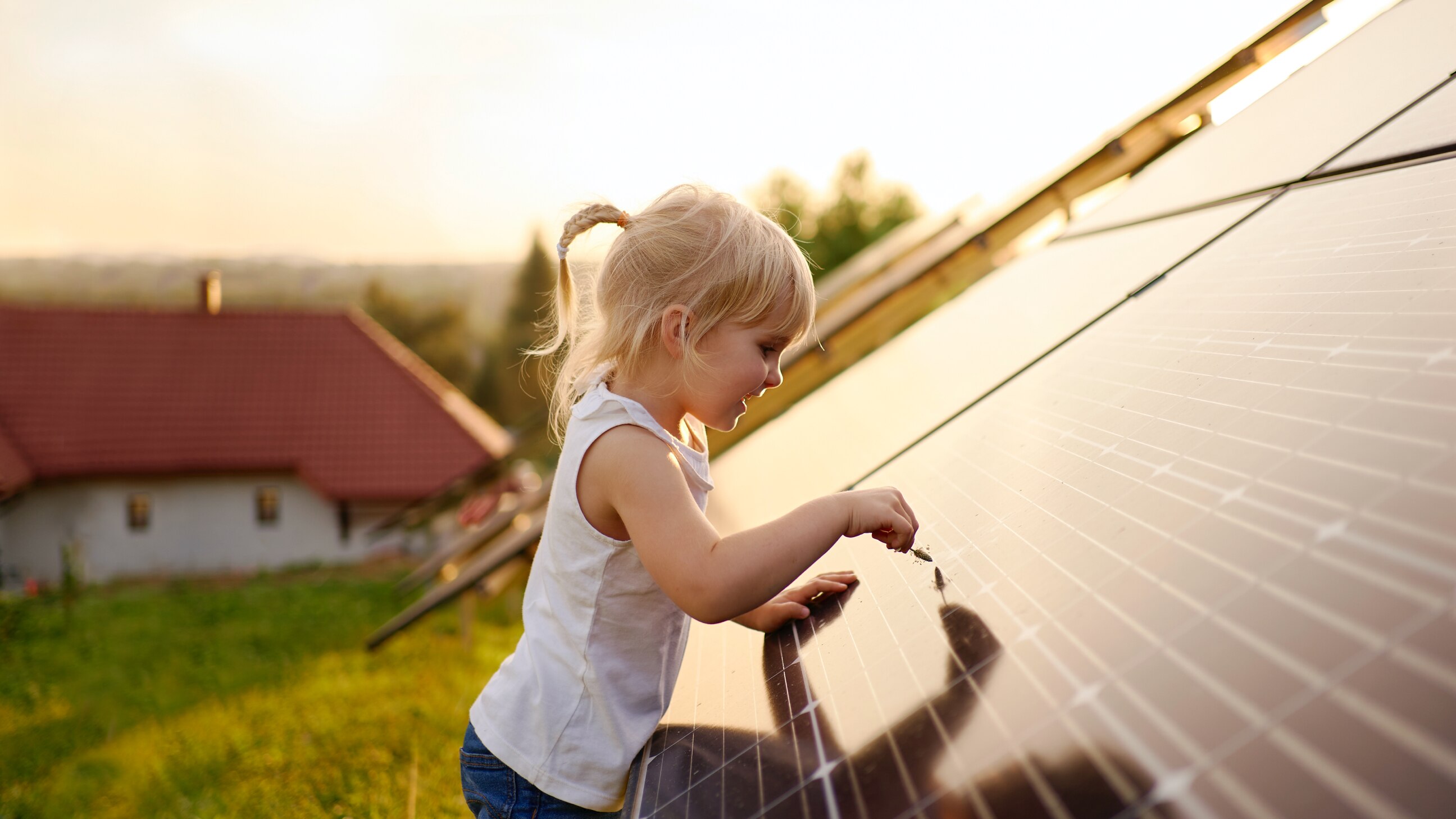 Little girl up close interacting with a solar panel outdoors. Her house is seen in the background.