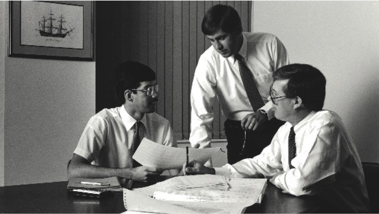 Three men holding a discussion around a conference table.