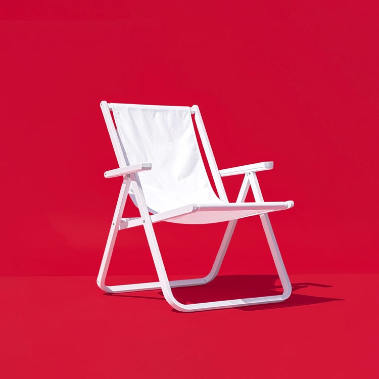 White folding beach chair with fabric seat and backrest, set against a solid bright red background.