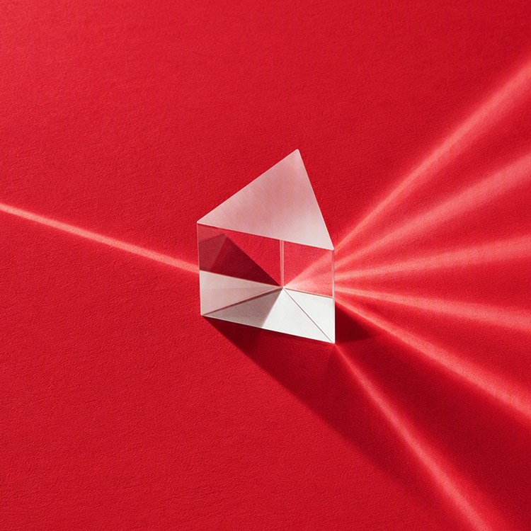 Clear glass prism on a red surface refracting a single beam of light into multiple light beams.