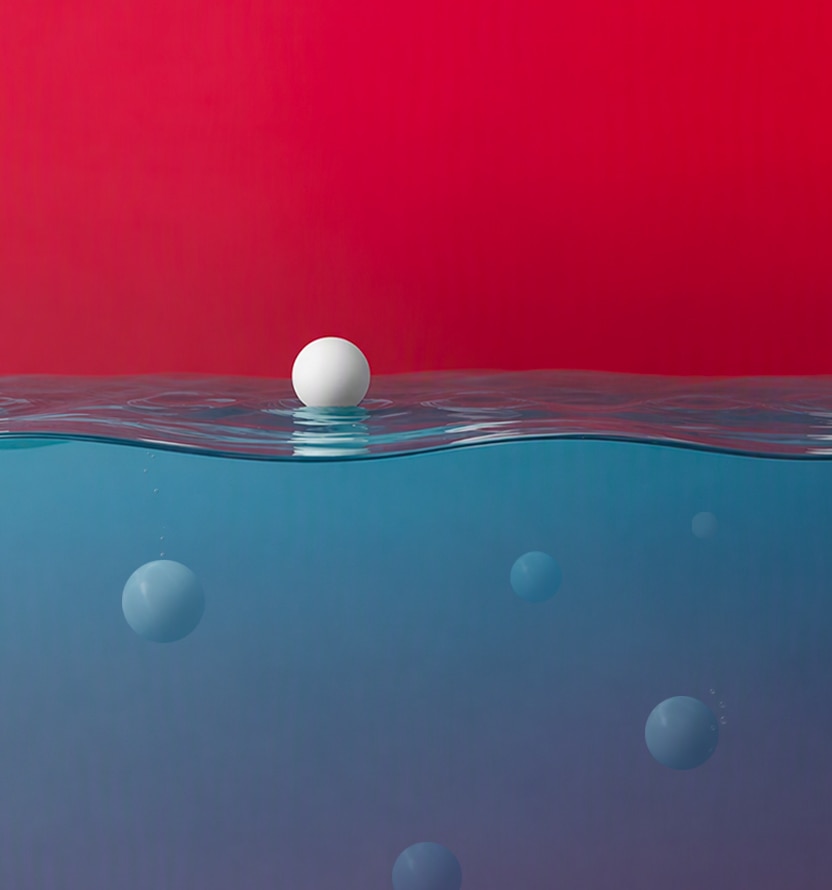 White sphere floating on a calm water surface, with several blurred spheres visible underwater against a red-to-blue gradient background.