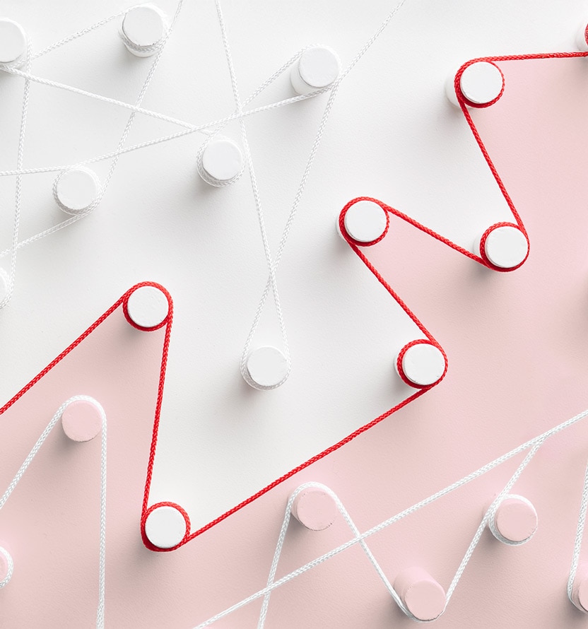 Abstract image of red and white cords woven in zigzag patterns around circular pegs on a soft pink and light gray background. The cords create intersecting geometric lines across the image, with the red cord standing out prominently against the muted pastel colors. The composition has a clean, minimalist design and conveys the idea of interconnected paths or processes.