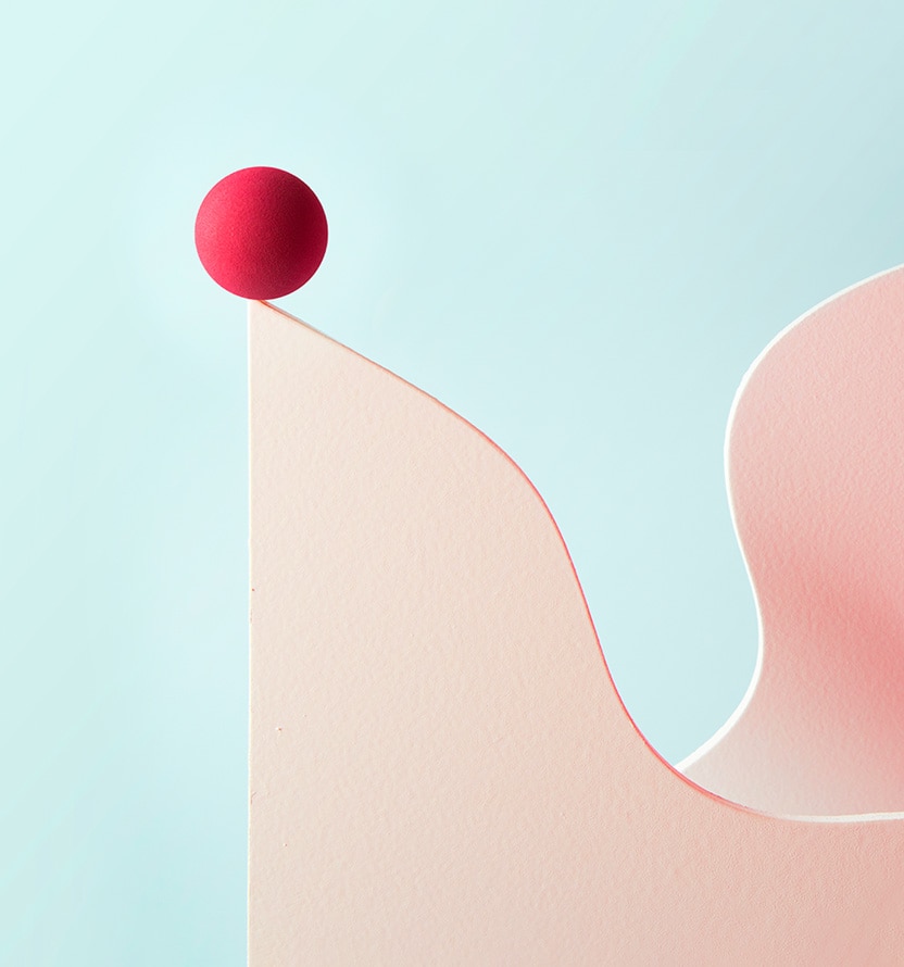 Abstract minimalist illustration showing a smooth, curved vertical surface in soft pink tones against a pale blue background. A small red sphere rests at the top edge of the curved form, while another rounded pink shape rises on the right, creating a sense of balance, motion, and gentle contrast