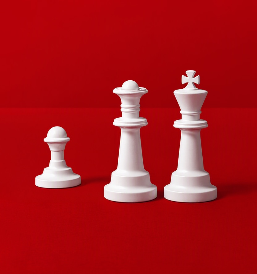 Three white chess pieces stand against a bright red background: a pawn on the left, a queen in the center, and a king on the right. The pieces are arranged in ascending height, with the king as the tallest piece, creating a simple, high-contrast composition.