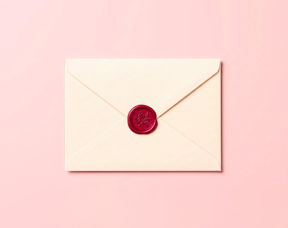 Cream envelope sealed with a red wax stamp on a pink background.