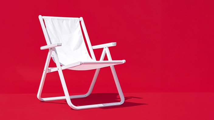 White folding beach chair on a solid red background