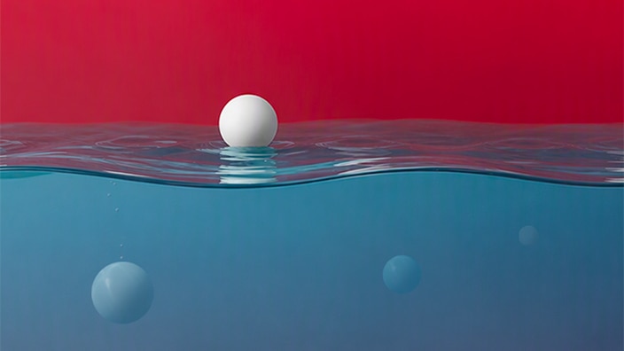 White sphere floating on a calm water surface, with several blurred spheres visible underwater against a red-to-blue gradient background.