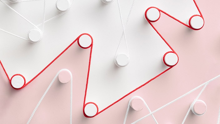Abstract image of red and white cords woven in zigzag patterns around circular pegs on a soft pink and light gray background. The cords create intersecting geometric lines across the image, with the red cord standing out prominently against the muted pastel colors. The composition has a clean, minimalist design and conveys the idea of interconnected paths or processes.