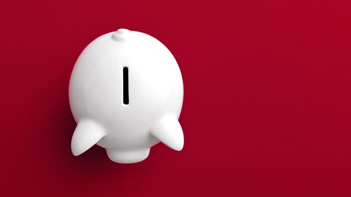 White ceramic piggy bank viewed from above on a solid red background, with a coin slot centered on its back.