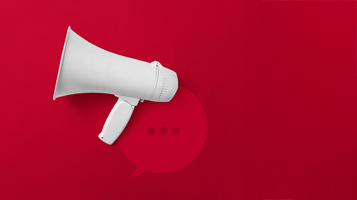 White megaphone positioned on a bright red background, with a subtle speech bubble icon and three dots behind it, symbolizing communication, announcements, or messaging.