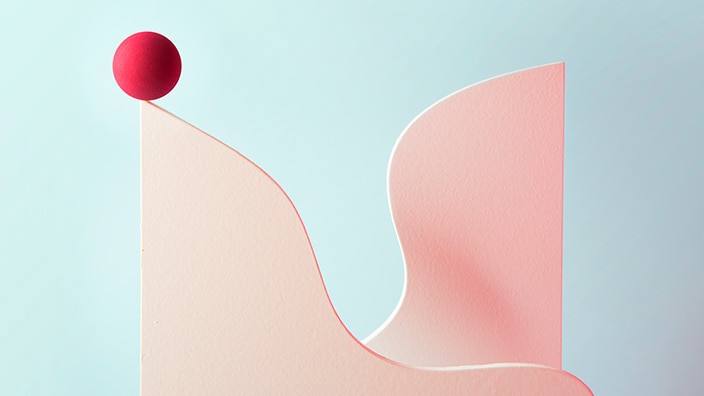 Abstract minimalist illustration showing a smooth, curved vertical surface in soft pink tones against a pale blue background. A small red sphere rests at the top edge of the curved form, while another rounded pink shape rises on the right, creating a sense of balance, motion, and gentle contrast.