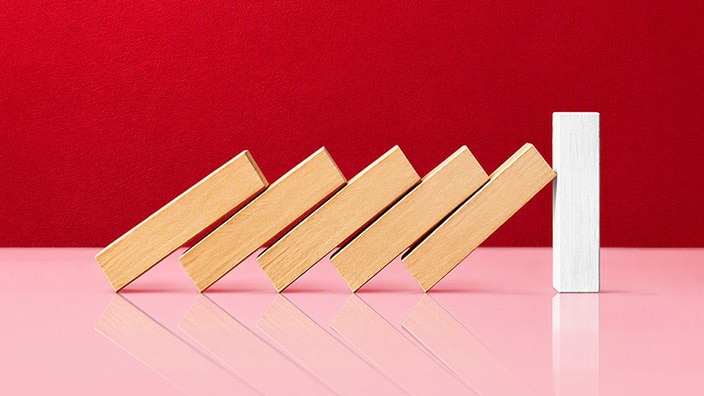 A row of wooden blocks leaning like falling dominoes against a single upright white block on a red background.