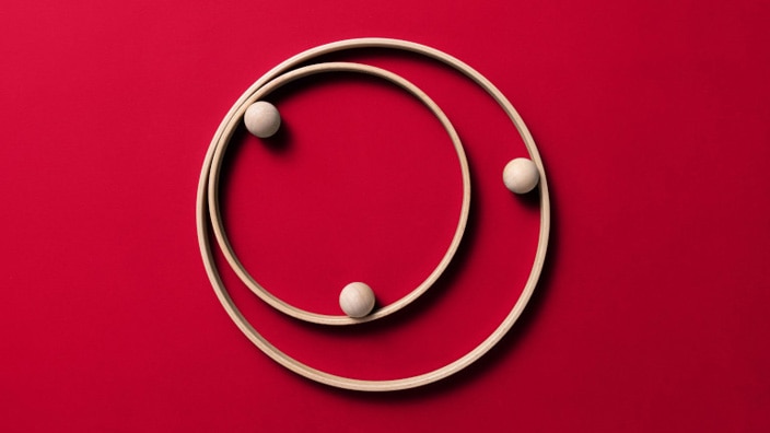 Three light-colored spheres positioned along two concentric circular tracks against a red background.